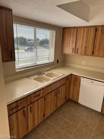 Kitchen with brown cabinetry, light countertops, dishwashing machine, dark tile patterned floors, and a textured ceiling