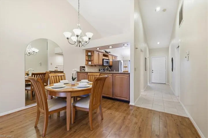 Dining space featuring suspended lighting, light wood-type flooring, arched walkways, and vaulted ceiling