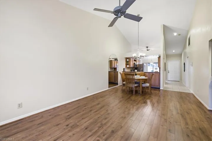Dining space with dark wood-type flooring, lofted ceiling, ceiling fan, hanging lights, and arched walkways