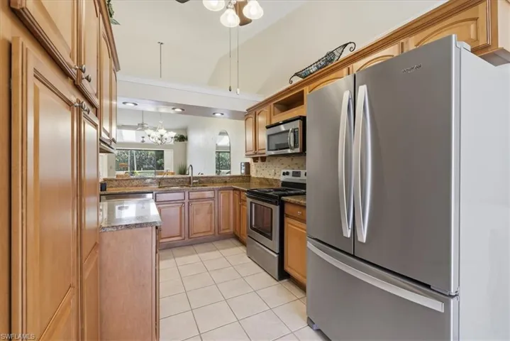 Kitchen featuring stainless steel appliances, dark stone countertops, light tile patterned floors, ceiling fan, and wood finish cabinets