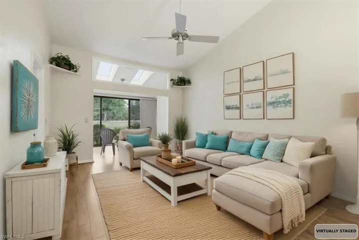 Living room featuring vaulted ceiling, hardwood / wood-style flooring, a skylight, and a ceiling fan
