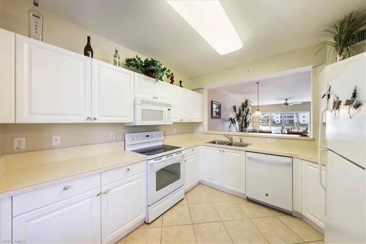 Kitchen with sink, white appliances, light tile patterned floors, ceiling fan, and white cabinets