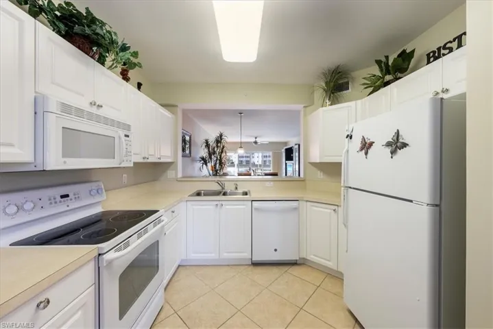Kitchen with white cabinetry, sink, light tile patterned flooring, and white appliances