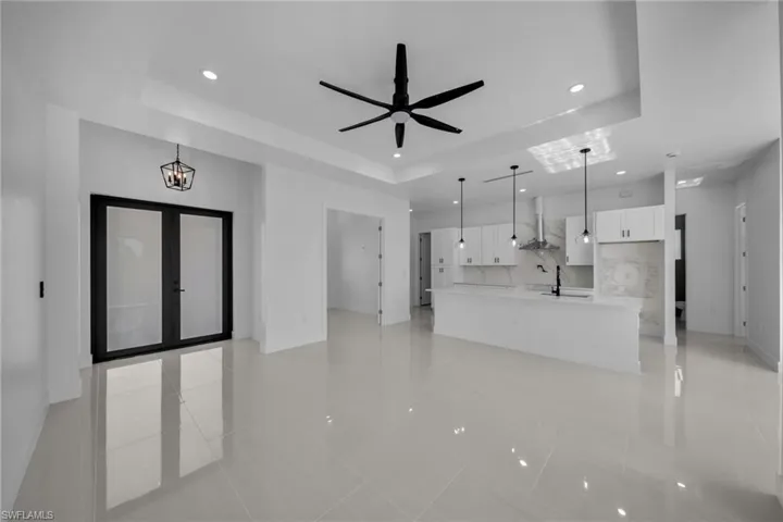 Unfurnished living room with a tray ceiling, light tile patterned flooring, recessed lighting, french doors, and ceiling fan