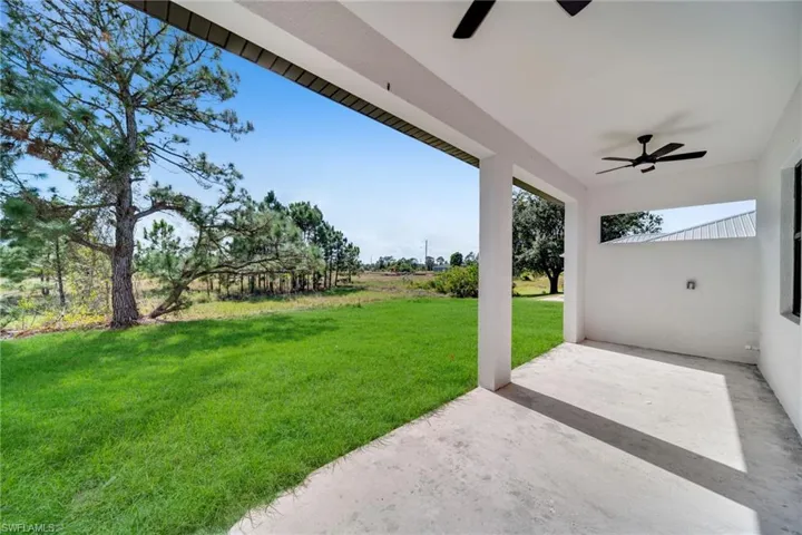 View of green lawn with a ceiling fan and a patio area