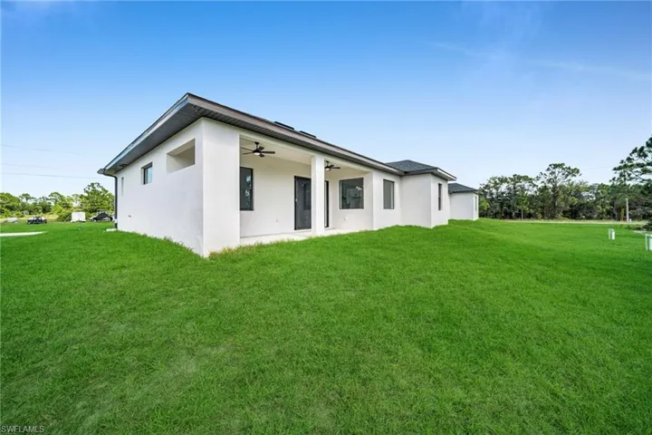 Back of house featuring ceiling fan, stucco siding, a yard, and a patio area