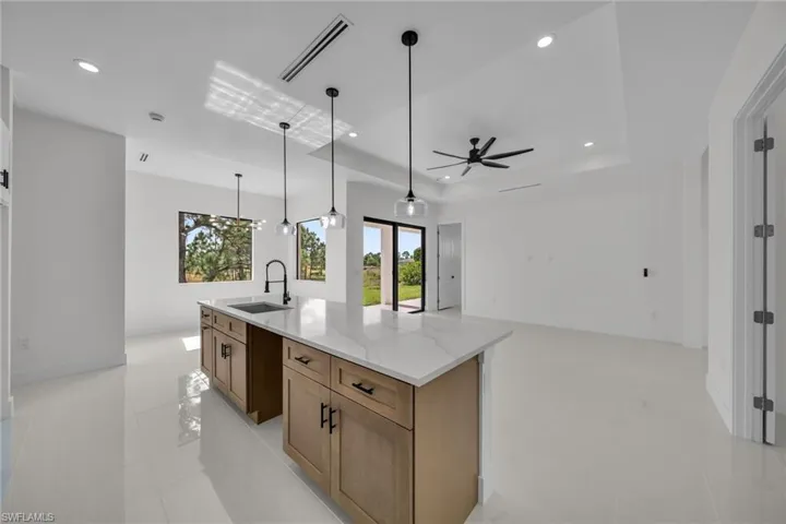 Kitchen featuring light stone countertops, brown cabinetry, recessed lighting, light tile patterned floors, and hanging light fixtures