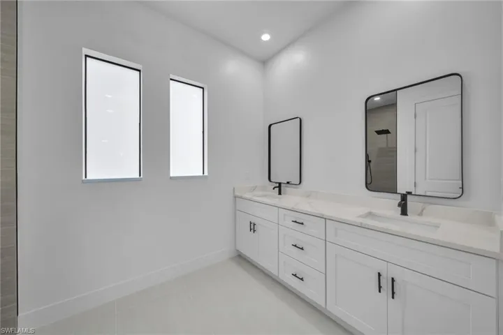 Bathroom featuring double vanity, light tile patterned floors, tiled shower, and recessed lighting