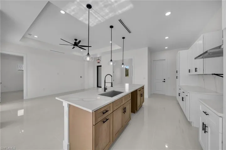 Kitchen featuring white cabinets, light stone counters, light tile patterned flooring, open floor plan, and a large island with sink