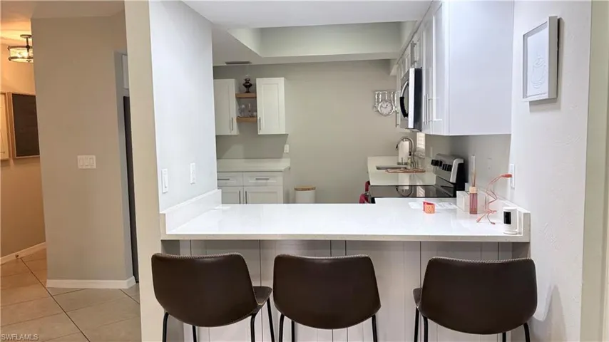 Kitchen featuring white cabinets, electric range oven, a peninsula, a kitchen breakfast bar, and stainless steel microwave