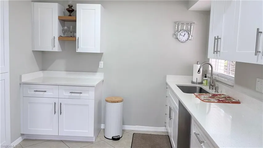 Kitchen with white cabinetry, light stone counters, open shelves, light tile patterned floors, and stainless steel dishwasher