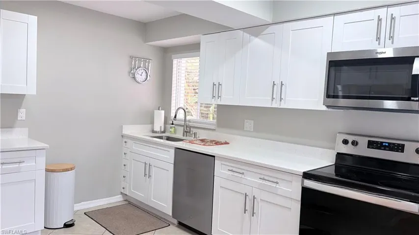 Kitchen featuring stainless steel appliances, white cabinetry, light stone countertops, and light tile patterned floors