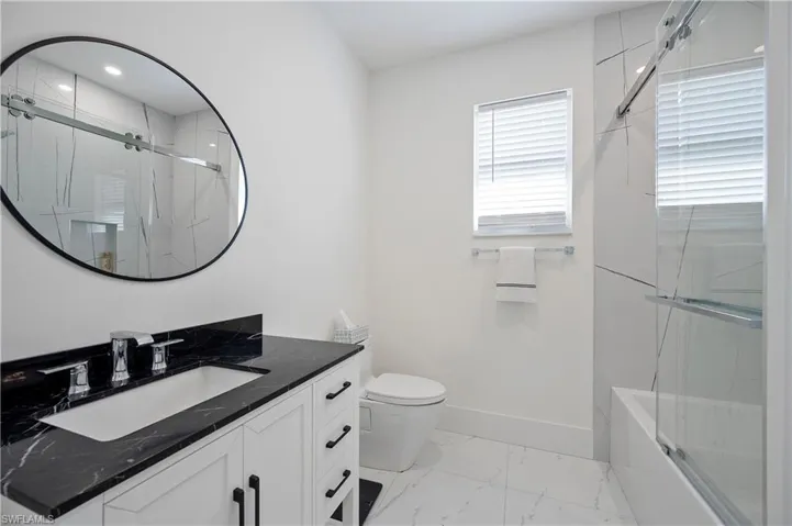 Bathroom with vanity, bath / shower combo with glass door, toilet, marble finish floor, and baseboards