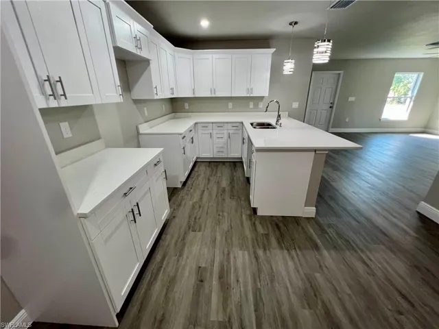 Kitchen with pendant lighting, sink, white cabinets, and a center island with sink