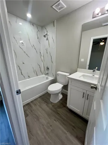 Full bathroom with vanity, tiled shower / bath combo, wood-type flooring, and toilet