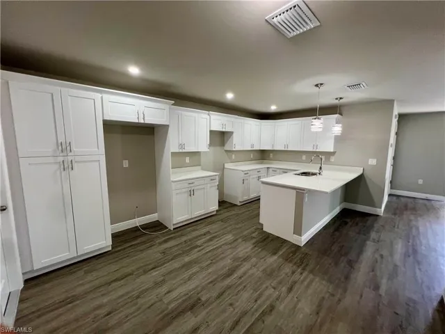 Kitchen featuring pendant lighting, dark wood-type flooring, sink, and white cabinets