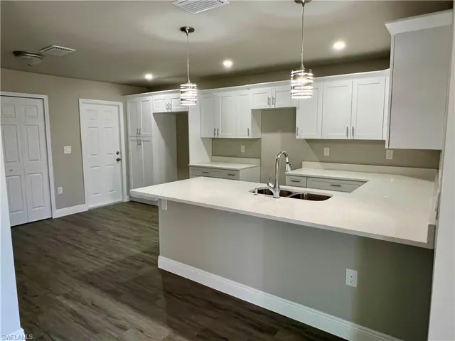 Kitchen featuring white cabinetry, decorative light fixtures, sink, and dark wood-type flooring