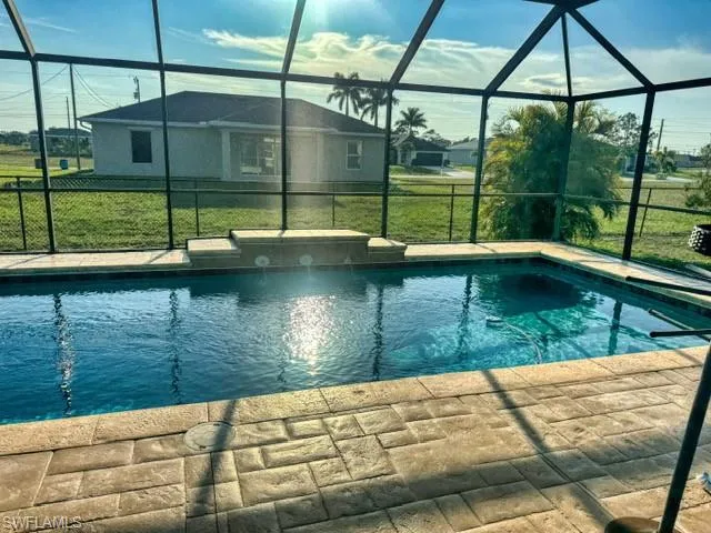 View of pool with glass enclosure, a patio area, and a lawn