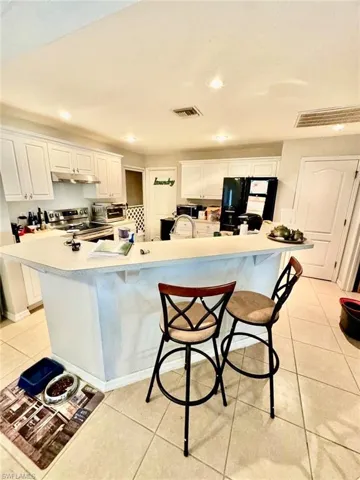 Kitchen with white cabinetry, black refrigerator with ice dispenser, a large island, and stainless steel range with electric stovetop