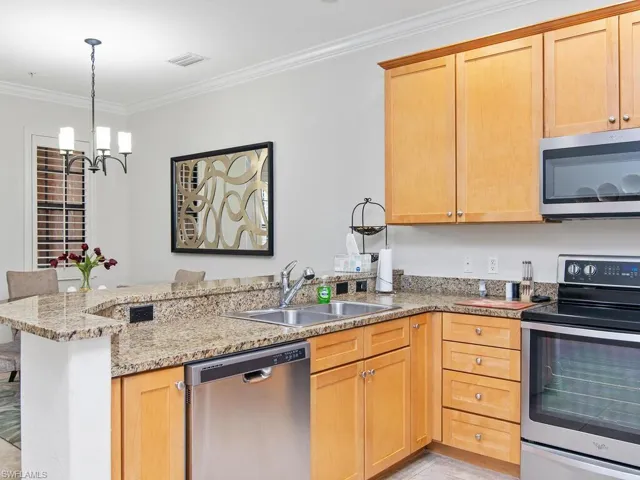 Kitchen featuring stainless steel appliances, a peninsula, ornamental molding, light stone countertops, and decorative light fixtures