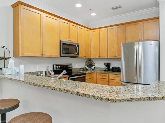 Kitchen with appliances with stainless steel finishes, light stone counters, a peninsula, crown molding, and recessed lighting