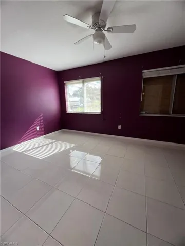 Light-toned ceramic tile flooring, ceiling fan with integrated lighting, dual windows with horizontal blinds, and smooth-finish walls