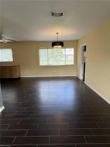 Living space featuring dark wood-finish tile flooring, a drum-style pendant light fixture, and horizontal window blinds