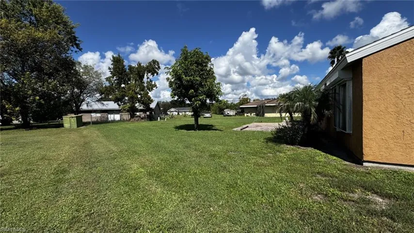Expansive backyard featuring a large grass lawn, mature trees, and a concrete slab foundation