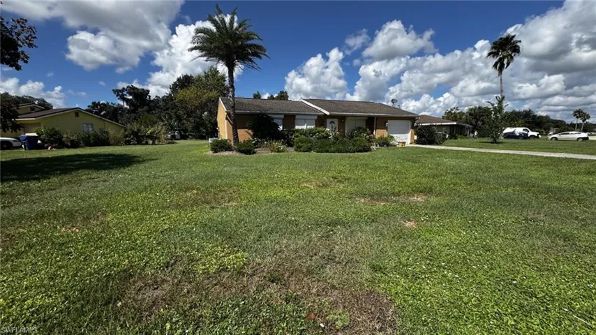 Single-story residence featuring a brick exterior, shingled roof, attached garage, and mature palm landscaping on a spacious lot
