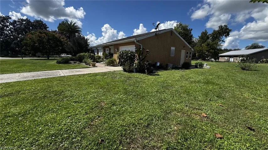 Stucco exterior residence featuring an attached garage, concrete driveway, and expansive lot with mature landscaping