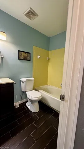 Bathroom featuring wood-finish flooring, a dark-toned vanity with a light-colored countertop, and a bathtub with tiled surround