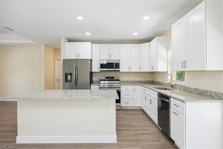 Kitchen with light hardwood / wood-style flooring, stainless steel appliances, a center island, and light stone countertops