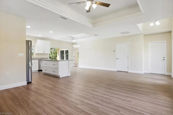 Unfurnished living room featuring light hardwood / wood-style floors, ceiling fan with notable chandelier, crown molding, and a raised ceiling