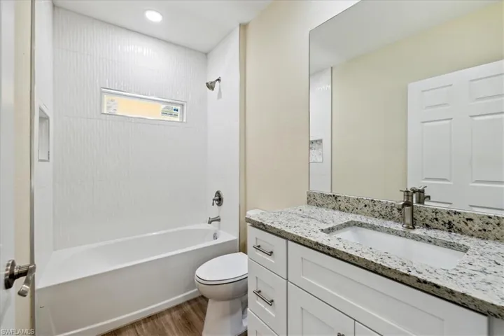 Full bathroom with hardwood / wood-style flooring, vanity, tiled shower / bath, and toilet