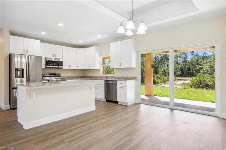 Kitchen with a raised ceiling, white cabinets, light stone countertops, light hardwood / wood-style floors, and stainless steel appliances
