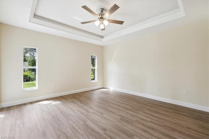 Spare room with ceiling fan, a raised ceiling, hardwood / wood-style flooring, and crown molding