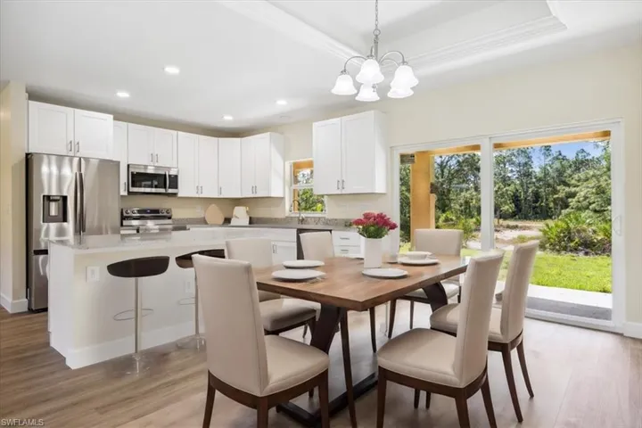 Dining space with sink, light wood-type flooring, a raised ceiling, and a notable chandelier