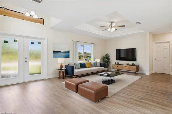Living room with ceiling fan, french doors, a tray ceiling, and wood-type flooring