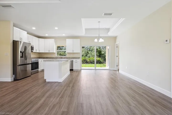 Kitchen with stainless steel appliances, white cabinets, light wood-type flooring, a tray ceiling, and a center island