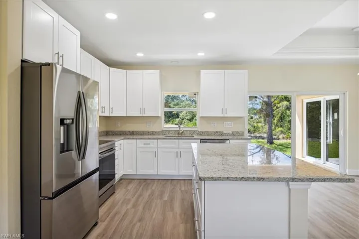 Kitchen with light stone countertops, light wood-type flooring, stainless steel appliances, and a wealth of natural light