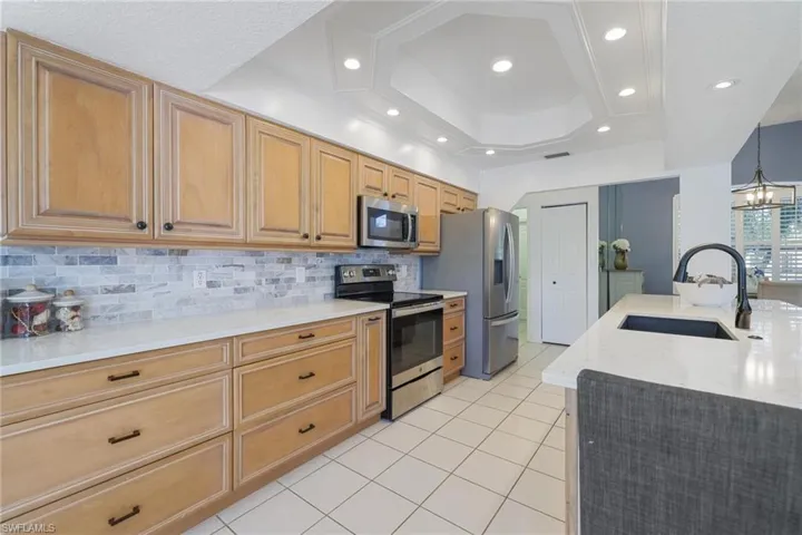 Kitchen with light stone countertops, stainless steel appliances, a chandelier, light tile patterned flooring, and recessed lighting