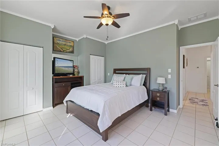 Bedroom featuring two closets, ornamental molding, light tile patterned flooring, and ceiling fan