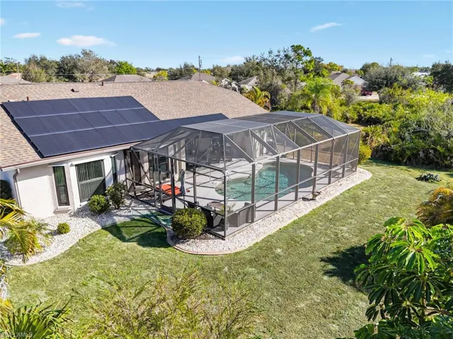 Rear view of house with an outdoor pool, glass enclosure, a shingled roof, a lawn, and a sunroom
