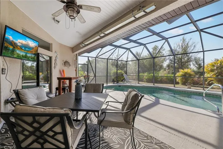 View of patio featuring a lanai, an outdoor pool, outdoor dining area, a sunroom, and ceiling fan