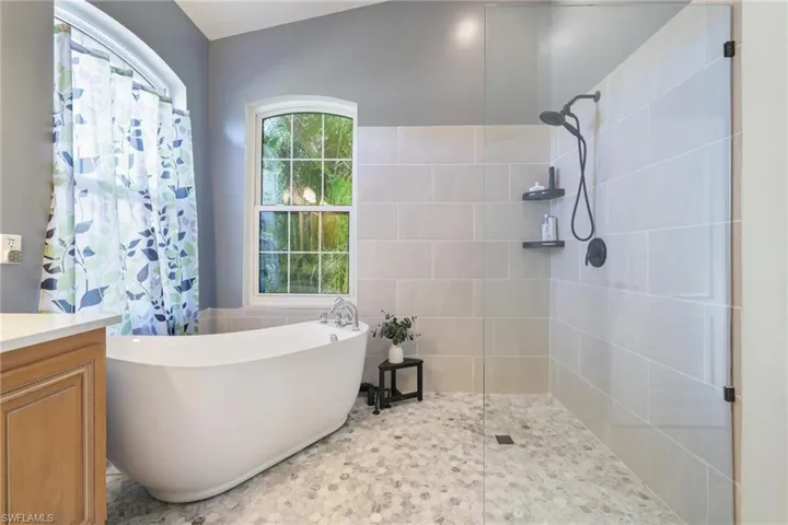 Bathroom with a walk in shower, tile walls, a freestanding bath, vanity, and a wainscoted wall