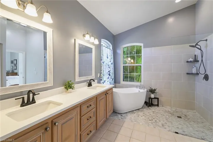 Bathroom featuring a walk in shower, a freestanding bath, vaulted ceiling, double vanity, and light tile patterned floors