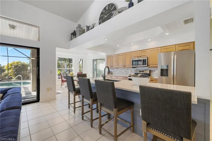 Kitchen with stainless steel appliances, a breakfast bar area, decorative backsplash, light stone counters, and a sunroom