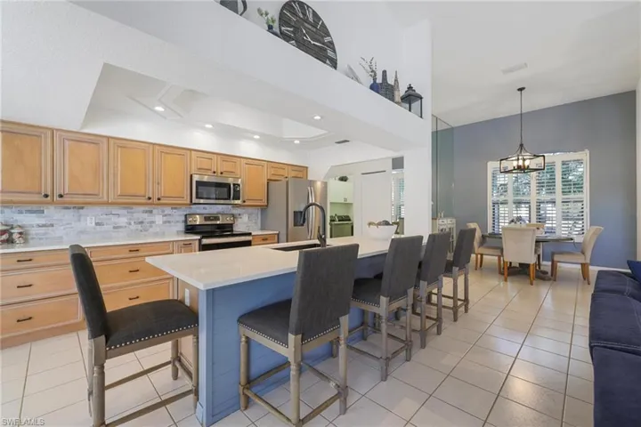 Kitchen featuring stainless steel appliances, a kitchen breakfast bar, pendant lighting, light stone countertops, and recessed lighting