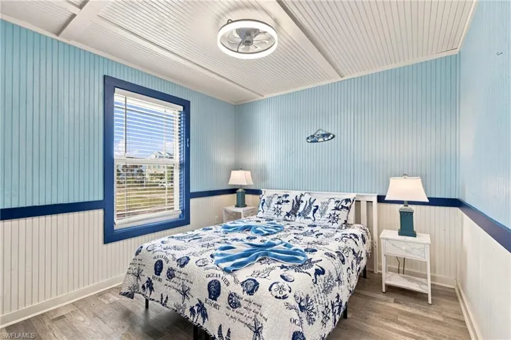Bedroom featuring beadboard wall paneling, a vaulted ceiling with integrated ceiling fan, and wood-finish flooring - Virtually Edited Image