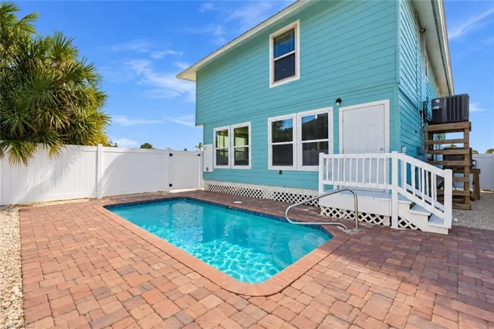 Exterior featuring lap siding, inground pool with brick paver surround, white vinyl privacy fencing, and elevated wooden deck with stairs - Virtually Edited Image